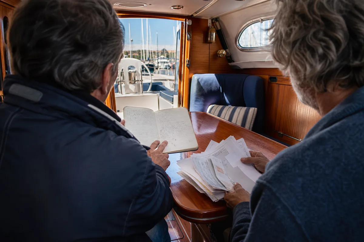 Un acheteur et un expert maritime examinant un carnet d&rsquo;entretien et des factures dans le carré d&rsquo;un voilier
