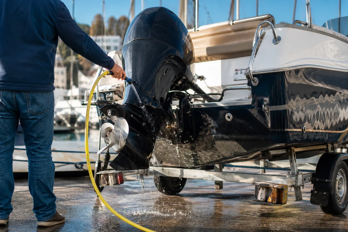 Un propriétaire rinçant le circuit d’eau de mer de son moteur hors-bord, bateau posé sur sa remorque après la sortie